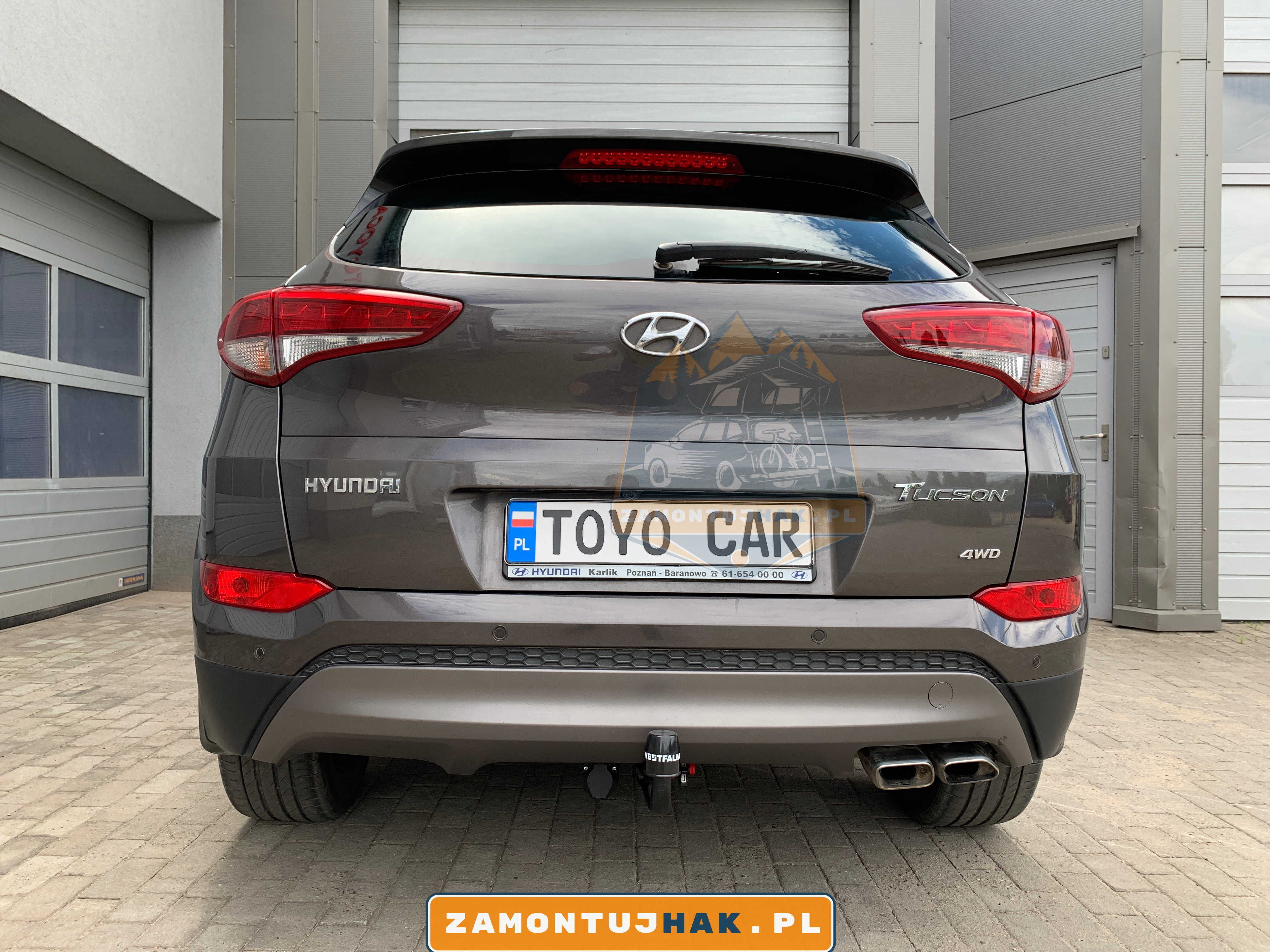 Zdjęcie Hyundaia Tucsona z zamontowanym hakiem holowniczym westfalia A40V, zdjęcie zostało zrobione z tyłu samochodu, na tle serwisu zamontujhak.pl